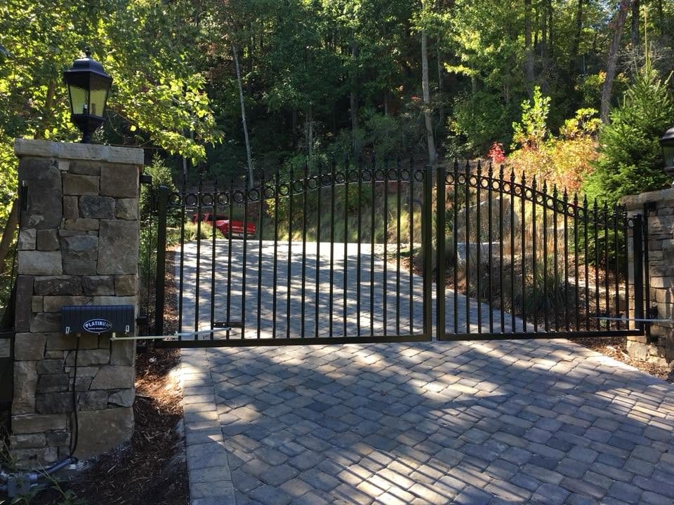 Swing gate operator on a stone pillar driving a black iron double gate
