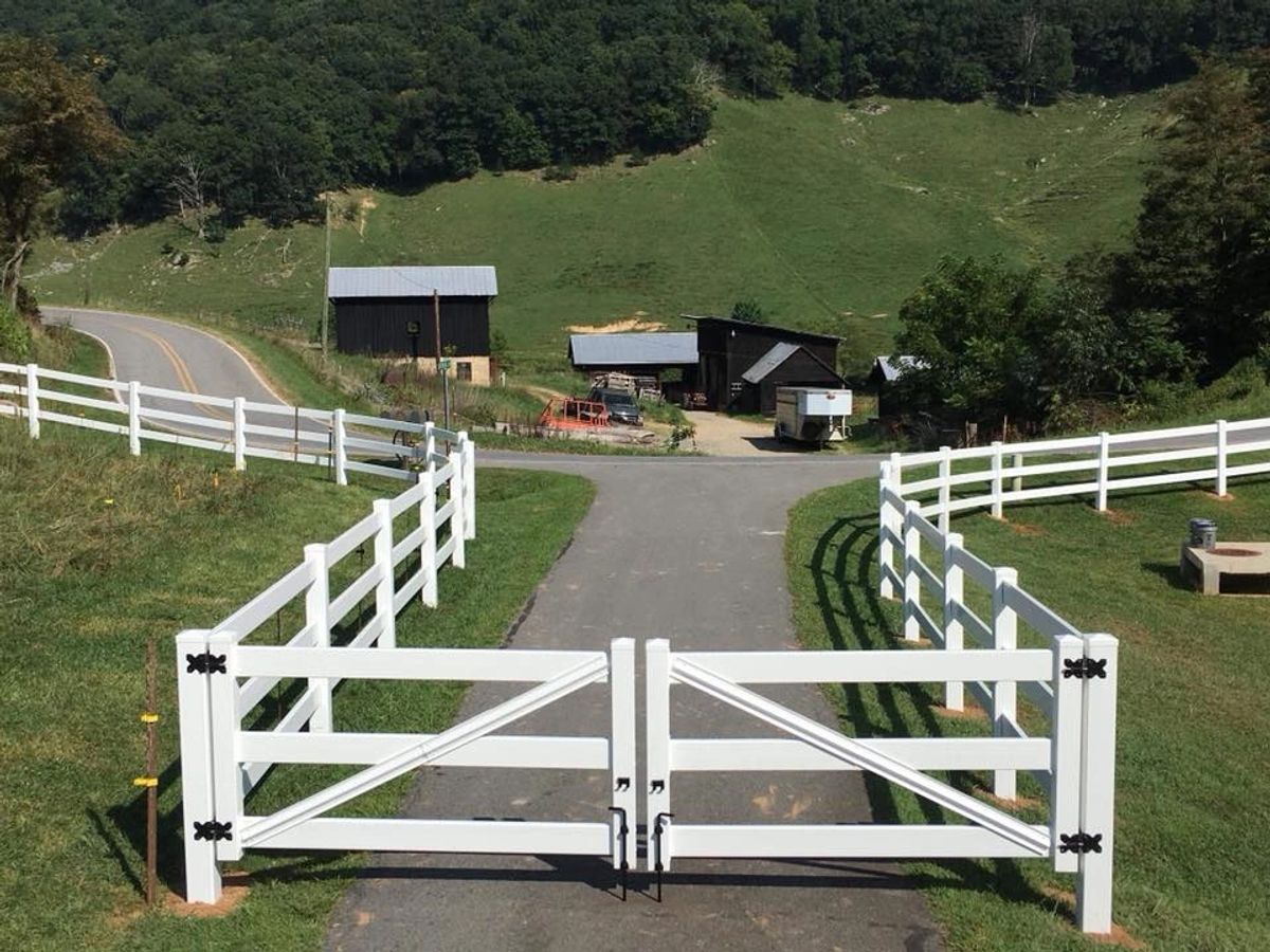 White vinyl three-rail double driveway gate on a farm